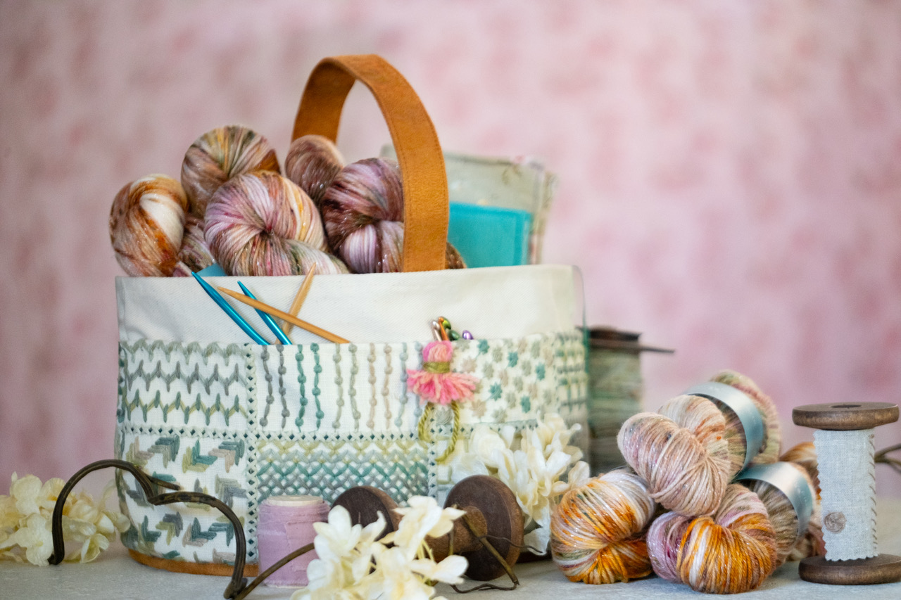 An Atenti Lily Caddy plus skeins of colorful hand-dyed yarn against a light pink background