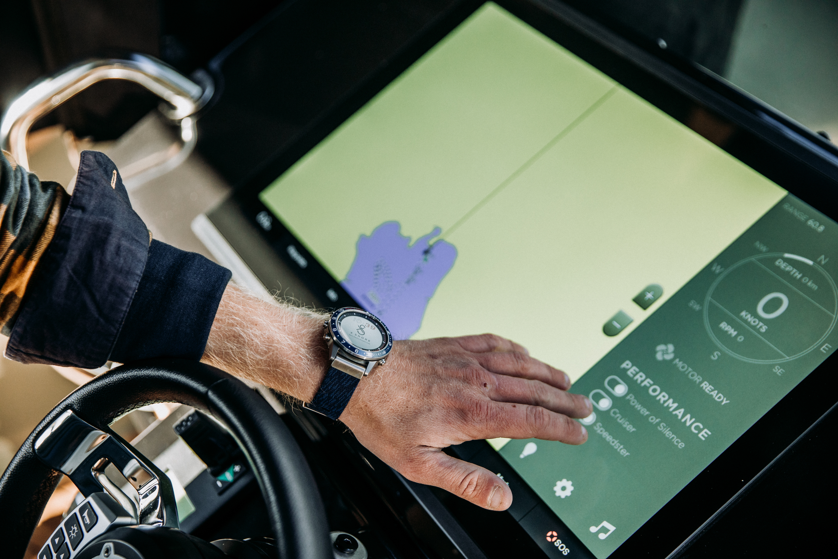 A hand touching the screen with the X Shore Garmin Watch on the wrist