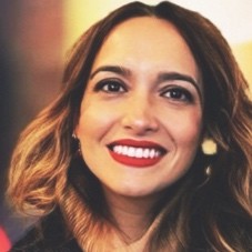 Luciane é uma mulher branca, com cabelos lisos e loiros escuros. Está usando batom vermelho.