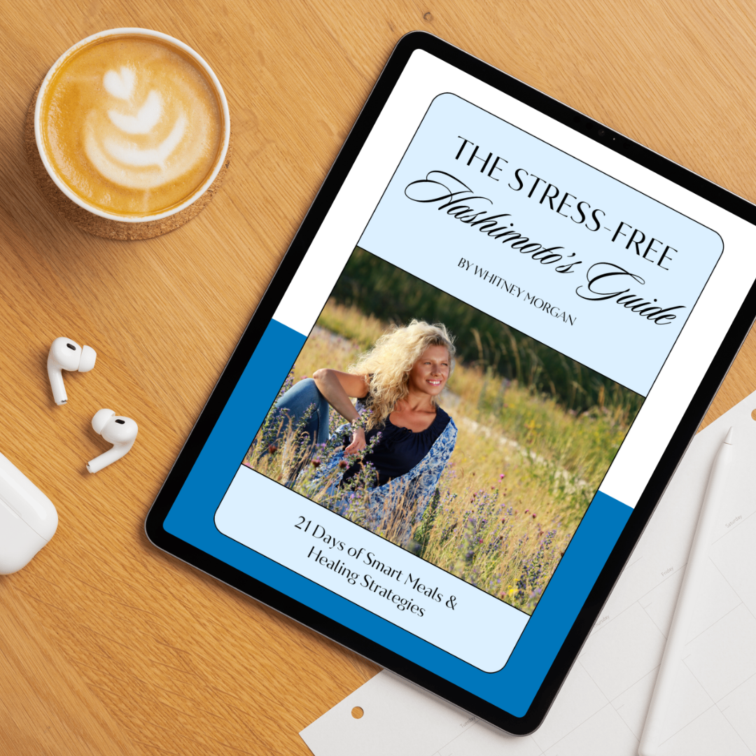 Tablet displaying the cover of “The Stress-Free Hashimoto’s Guide” by Whitney Morgan, featuring a woman sitting in a wildflower field. Text on the cover reads: “21 Days of Smart Meals & Healing Strategies.” A latte and AirPods sit nearby on a wooden desk.
